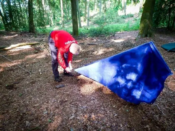 Tarp-Notunterkunft wird mit Heringen im Wald befestigt