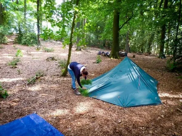 Tarp-Notunterkunft wird mit Zweigen gesichert