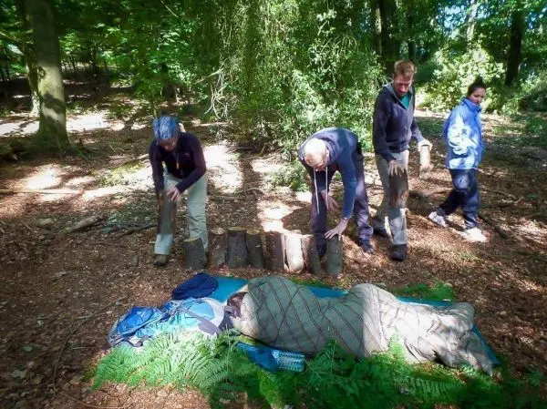 Teilnehmer bauen eine improvisierte Trage aus Holzstücken im Wald