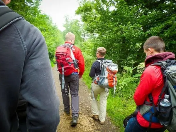 Wanderer mit Rucksäcken gehen einen schmalen Weg entlang, umgeben von Bäumen