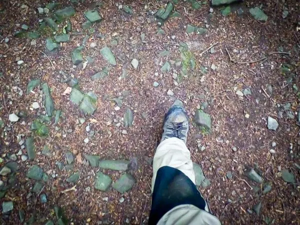 Wanderstiefel tritt auf einen steinigen, erdigen Weg mit Laub
