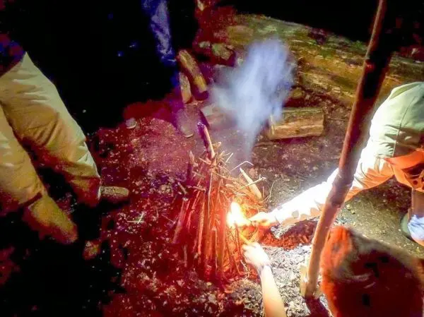 Zunder glimmt in einem kleinen Bodenfeuer, Hände halten Feuerstahl