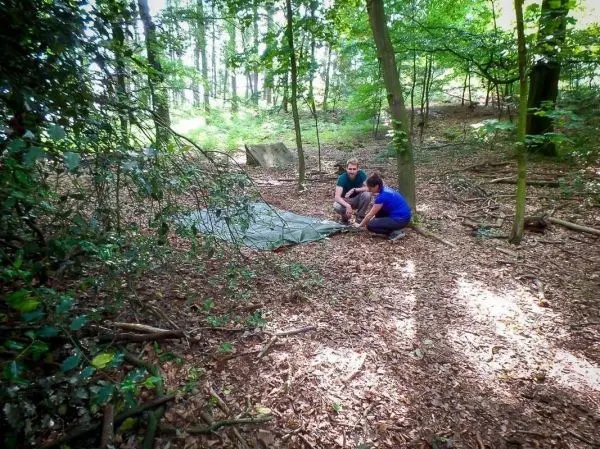 Zwei Personen bauen eine Tarp-Notunterkunft im Wald auf