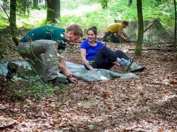 Zwei Personen bereiten eine Tarp-Notunterkunft im Wald vor