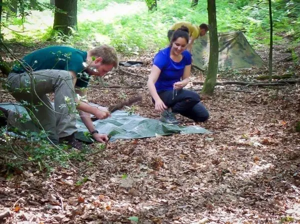 Zwei Personen bereiten eine Tarp-Notunterkunft im Wald vor