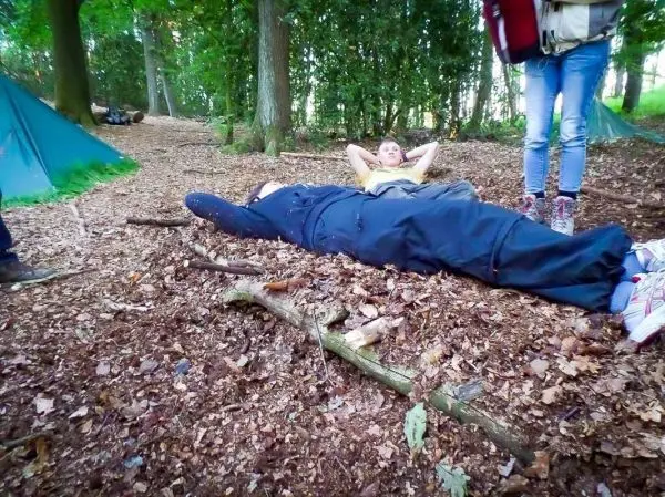 Zwei Personen liegen auf dem Waldboden, umgeben von Laub und Holzstücken