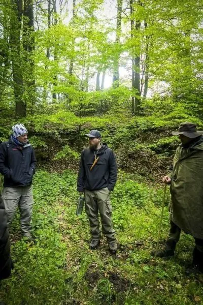 Drei Personen stehen im Wald und diskutieren über Überlebenstechniken