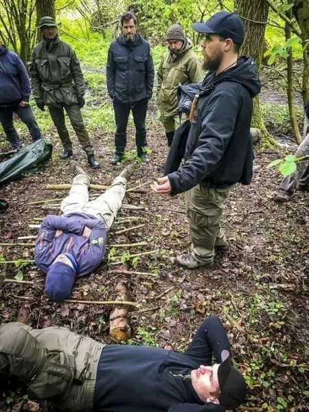 Ein Trainer erklärt eine Erste-Hilfe-Technik, während Teilnehmer auf dem Boden liegen