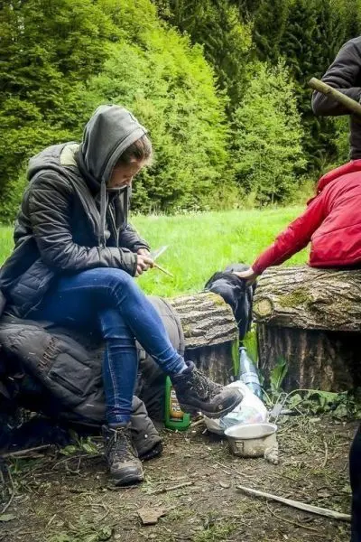 Frau schnitzt mit einem Messer an einem Holzstück, während ein anderer Teilnehmer neben ihr sitzt
