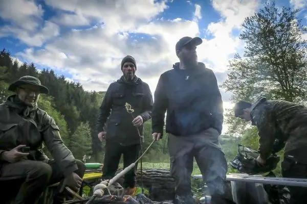 Grillspieße über einem kleinen Feuer, umgeben von Bäumen und Wolken