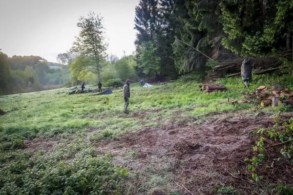 Grüne Wiese mit mehreren Tarp-Notunterkünften und Personen, die Holz sammeln