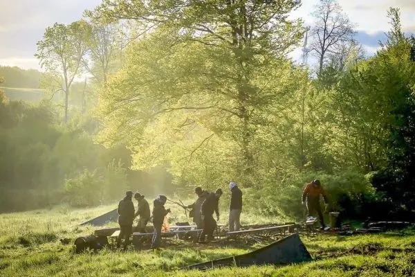 Gruppe arbeitet an einer Holzstruktur im Freien, umgeben von Bäumen und Wiese