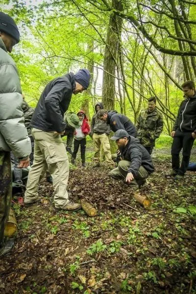 Gruppe beobachtet Anleitung zur Herstellung einer Schlagfalle im Wald