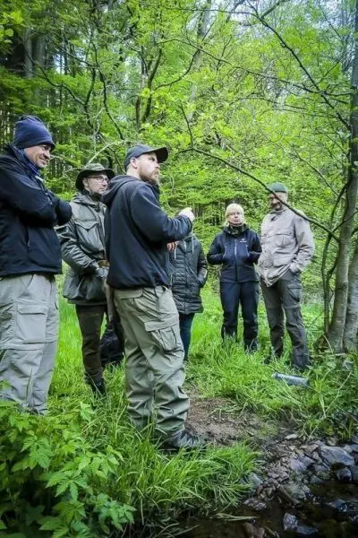 Gruppe diskutiert am Waldrand über Überlebenstechniken und Naturbeobachtungen