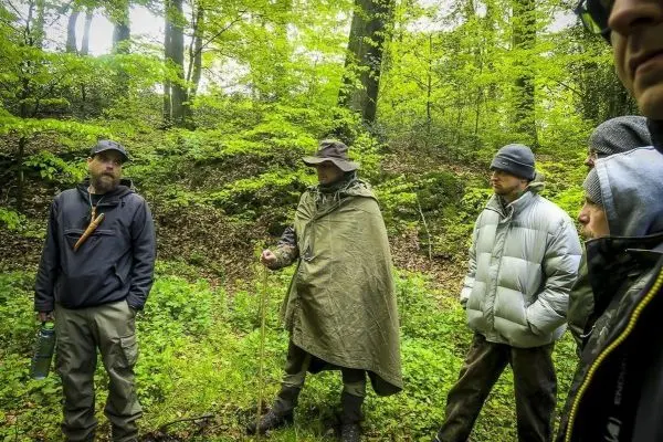 Gruppe diskutiert im Wald, einer hält einen Stock und spricht