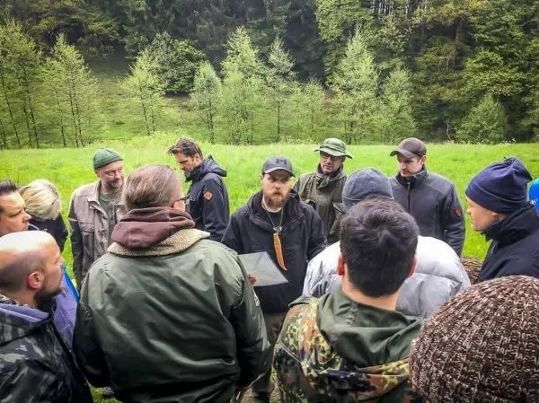 Gruppe diskutiert um einen Mann mit Karte in einer Waldlichtung