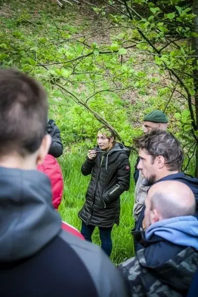 Gruppe hört einer Person im Wald aufmerksam zu, während sie etwas erklärt
