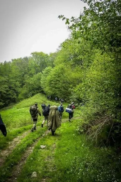 Gruppe mit Rucksäcken wandert einen schmalen Weg durch bewaldetes Gelände