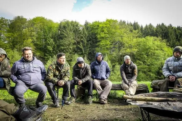 Gruppe sitzt auf Baumstämmen um ein kleines Bodenfeuer in der Natur