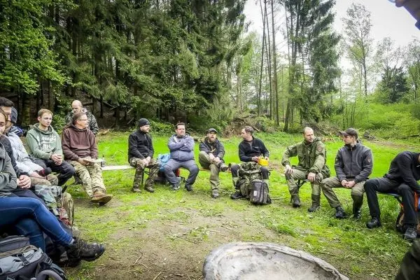 Gruppe sitzt auf einer Wiese im Wald und hört einem Vortrag zu