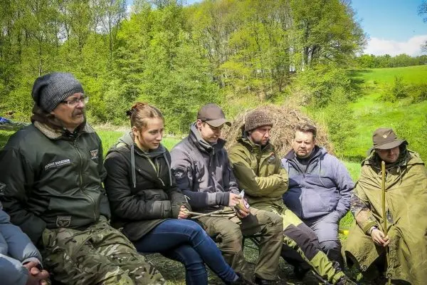 Gruppe sitzt im Freien auf Stühlen und hört aufmerksam zu