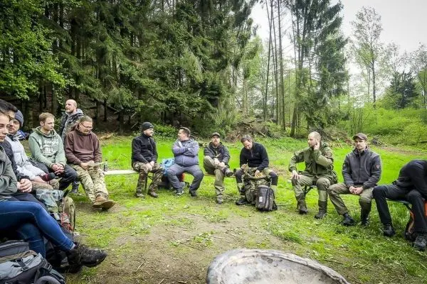 Gruppe sitzt im Kreis auf dem Boden in einem Waldgebiet