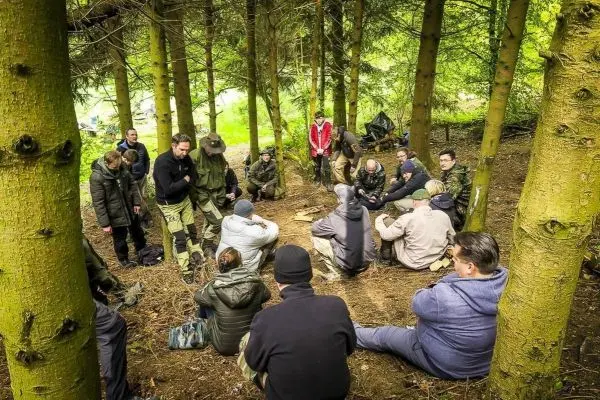 Gruppe sitzt im Wald auf dem Boden und beobachtet eine Demonstration