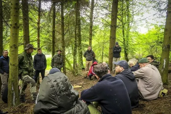 Gruppe sitzt im Wald auf dem Boden und hört einem Vortrag zu