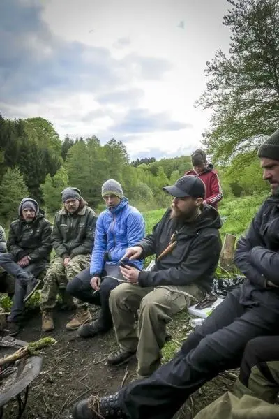 Gruppe sitzt um ein kleines Feuer und diskutiert verschiedene Techniken im Freien