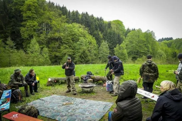 Gruppe sitzt um ein Lagerfeuer, während ein Teilnehmer Anweisungen gibt