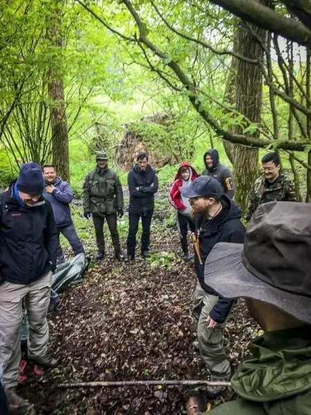 Gruppe steht im Wald um eine selbstgebaute Konstruktion aus Ästen