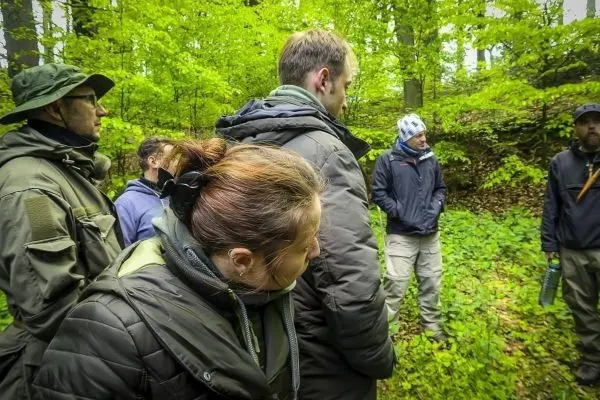 Gruppe steht im Wald und hört einem Vortrag zu, umgeben von grüner Vegetation