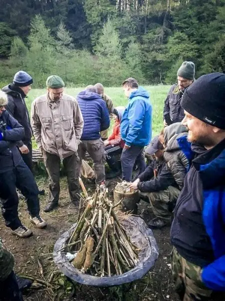 Gruppe um ein kleines Bodenfeuer versammelt, Holzstapel in der Mitte