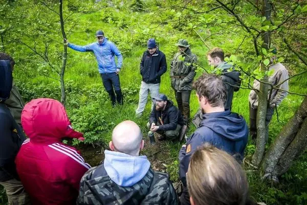 Gruppe um einen sitzenden Referenten im Wald versammelt, um Informationen auszutauschen