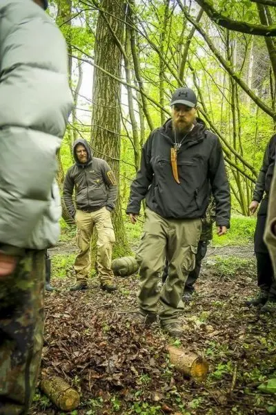 Gruppe von Personen im Wald, einer tritt auf einen Holzstamm