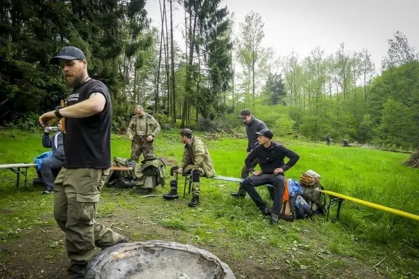 Gruppe von Personen mit Rucksäcken und Ausrüstung sitzt und steht im Wald