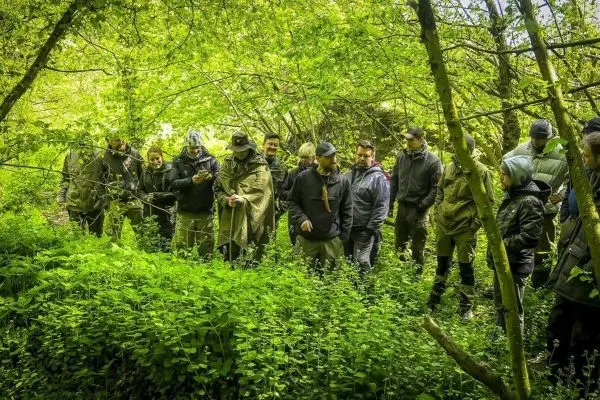 Gruppe von Personen steht im dichten Grün eines Waldes und betrachtet Karten