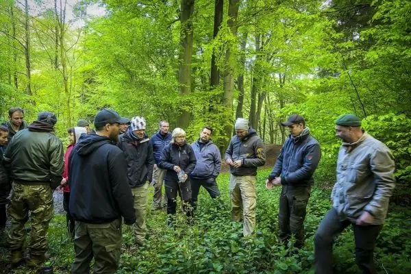 Gruppe von Personen steht im Wald und hört einem Vortrag zu