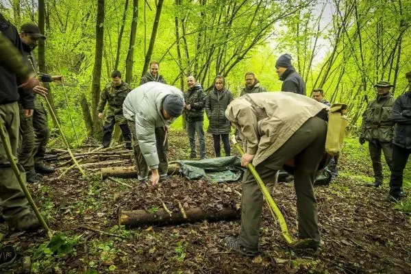 Gruppenteilnehmer bauen eine Tarp-Notunterkunft im Wald aus Ästen und Laub