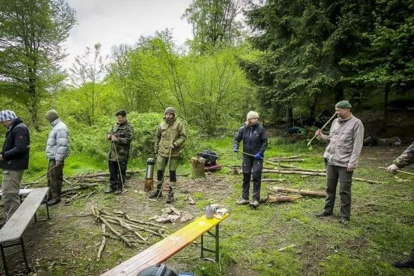 Gruppierung von Personen mit Stöcken in einem Waldgebiet, Holzstücke liegen verstreut