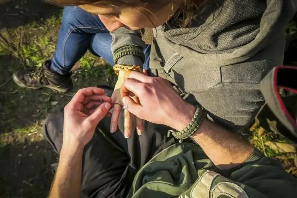 Hände binden ein Armband aus Paracord um das Handgelenk