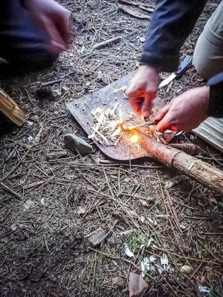 Hände zünden Zunder auf einer Schaufel im Wald beim Survival Training