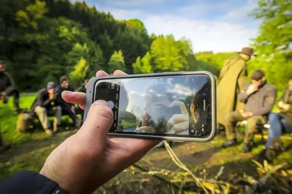Hand hält Smartphone, das eine Gruppe von Personen im Hintergrund zeigt