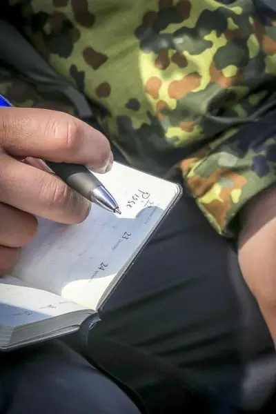 Hand schreibt mit einem Stift in ein Notizbuch mit Datumseintrag