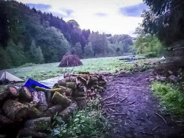Holzstapel und Tarp-Notunterkünfte in einer Waldlichtung