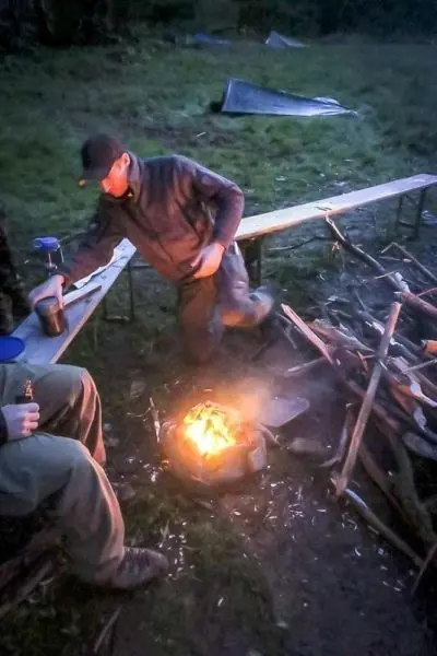 Kleine Flamme brennt in einem improvisierten Feuerplatz, Holzstapel daneben