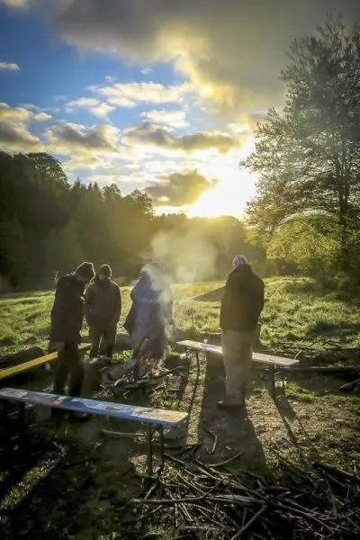 Kleines Bodenfeuer mit Rauch und umstehende Personen in der Natur