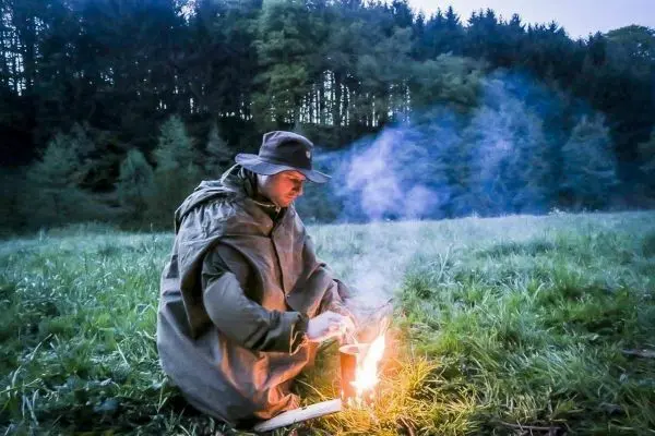 Kleines Bodenfeuer raucht neben einem Mann in wetterfester Kleidung