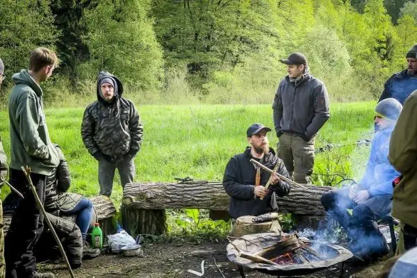 Lagerfeuer brennt in einer Feuerstelle, Teilnehmer sitzen auf Baumstämmen