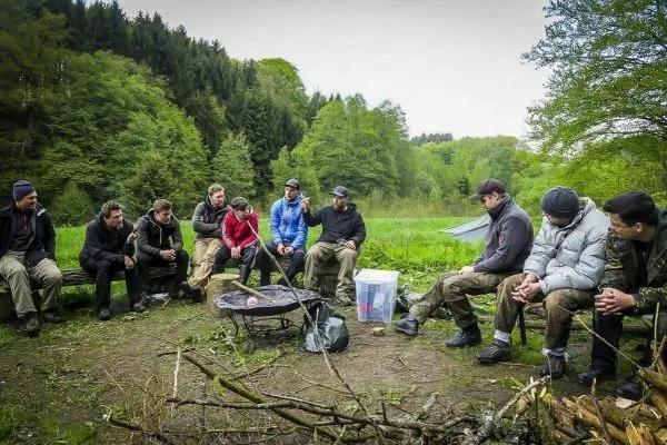 Lagerfeuer in der Mitte, Gruppe sitzt auf Baumstämmen und diskutiert